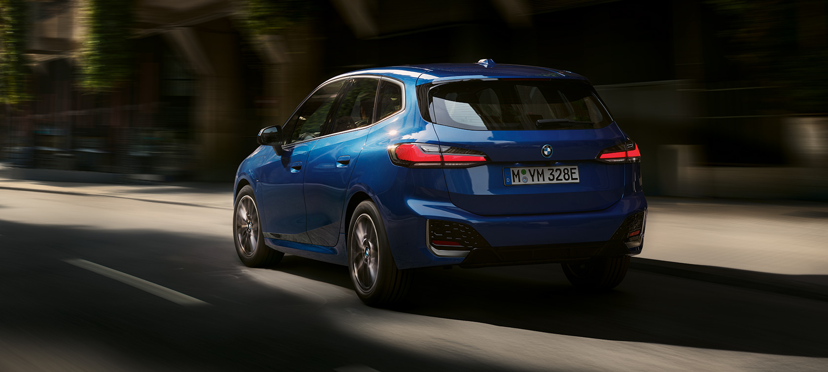 Plug-in hybridní BMW řady 2 Active Tourer 230e U06 2021 v metalické barvě M Portimao Blue (modrá) tříčtvrteční jízdní záběr zezadu ve městě