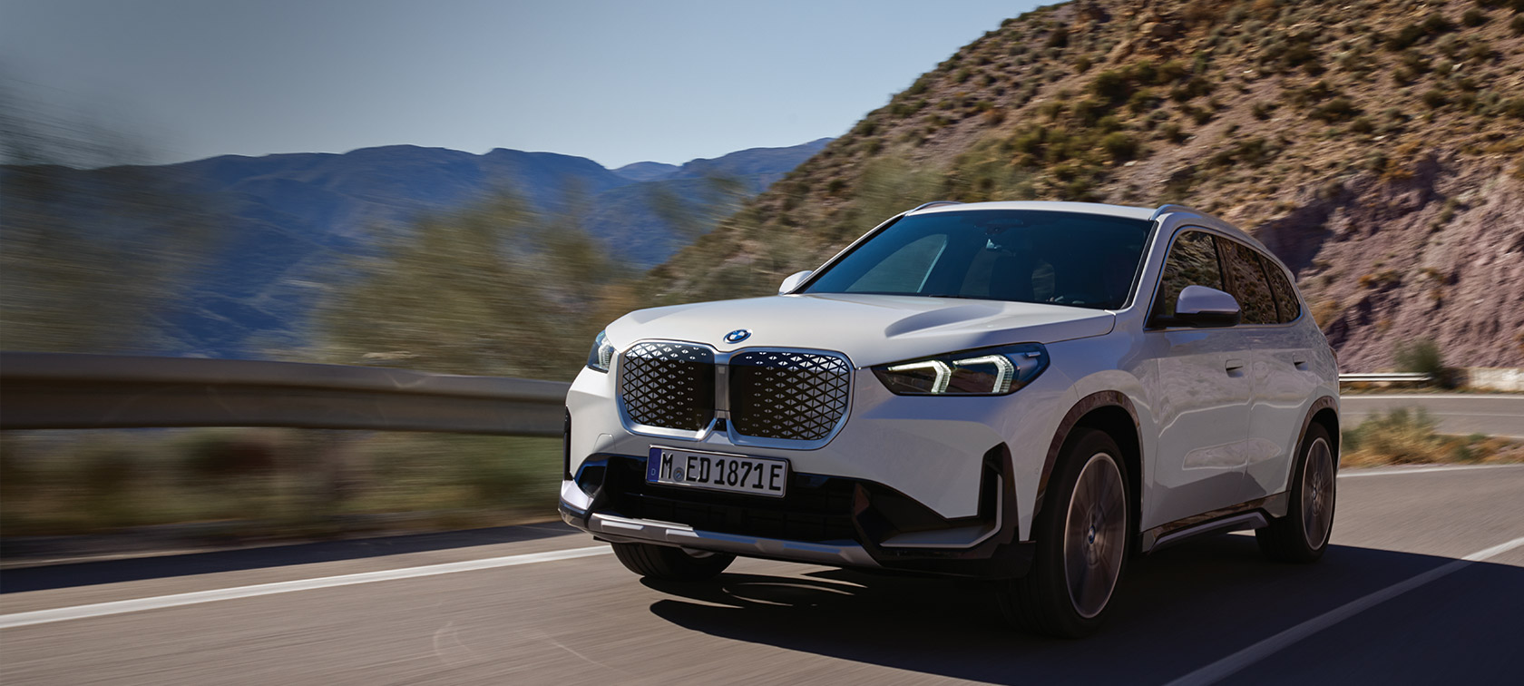 BMW iX1 U11 BEV 2022 metalický lak Mineral White tříčtvrteční pohled zepředu jízdní záběr na horských serpentinách